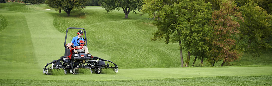 브랜드 Toro의 골프장 잔디 관리용 차를 탄 남자가 잔디를 깎고 있다.